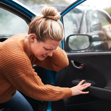 Woman holding her neck in pain while getting out of a car.